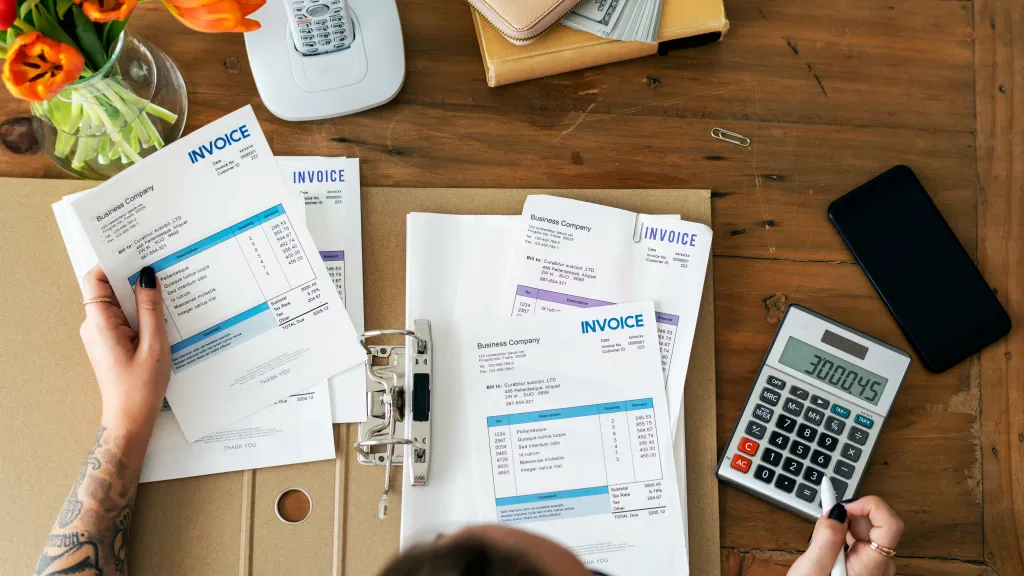A person sits at their desk with invoices and a calculator