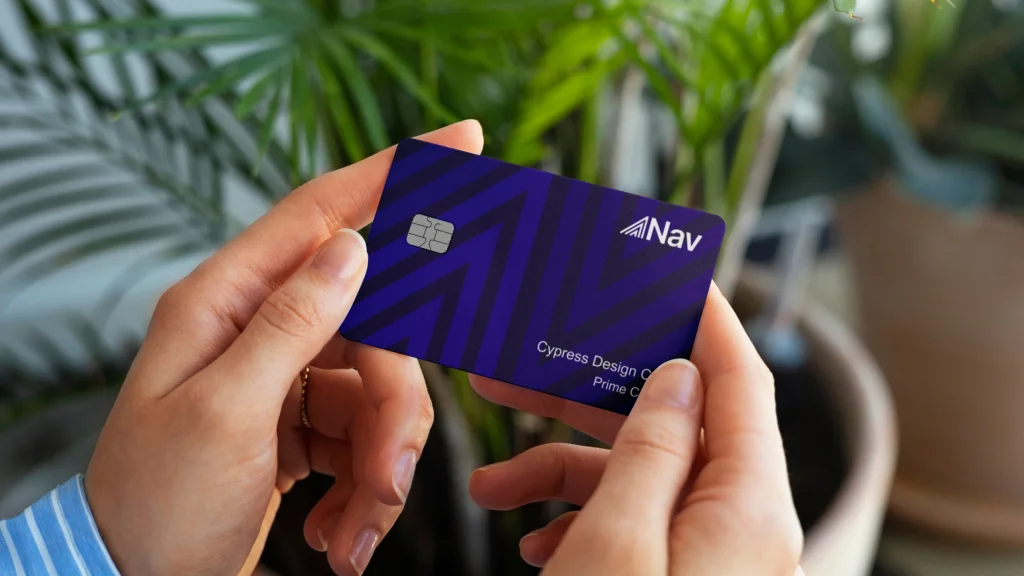 Hands holding a Nav Prime Card labeled "Cypress Design Co" with a background of indoor plants