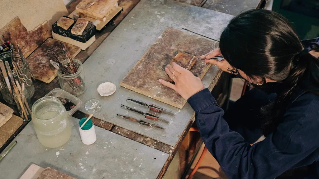 A person leans over a workshop table with woodworking tools in hand