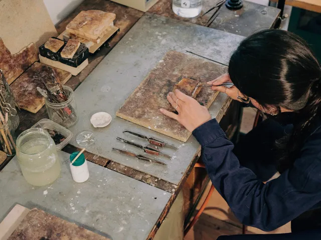 A person leans over a workshop table with woodworking tools in hand