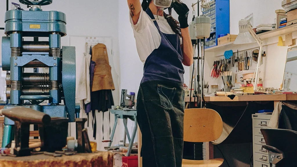 A woman in denim overalls attaches an industrial mask over her head