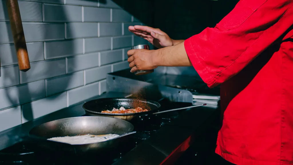 A pair of hands over a stove seasoning a dish