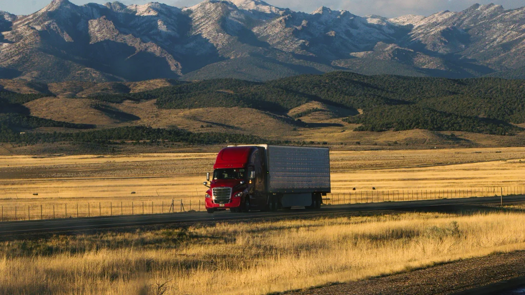 A truck drives down a road with snow-capped mountains in the background