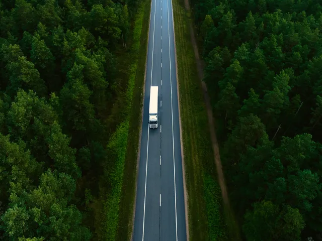 Overhead view of a truck on a long road surrounded by trees.