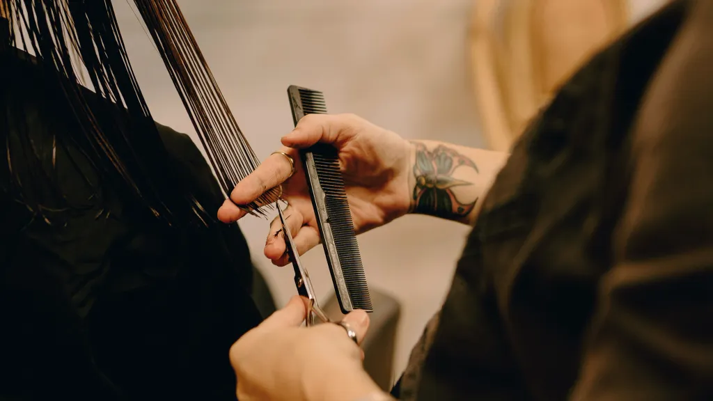 A barber holds a pair of scissors to a client's hair