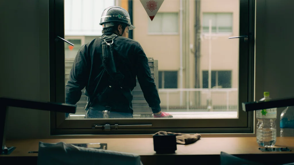 A man in a hard hat leans with his back against a window frame