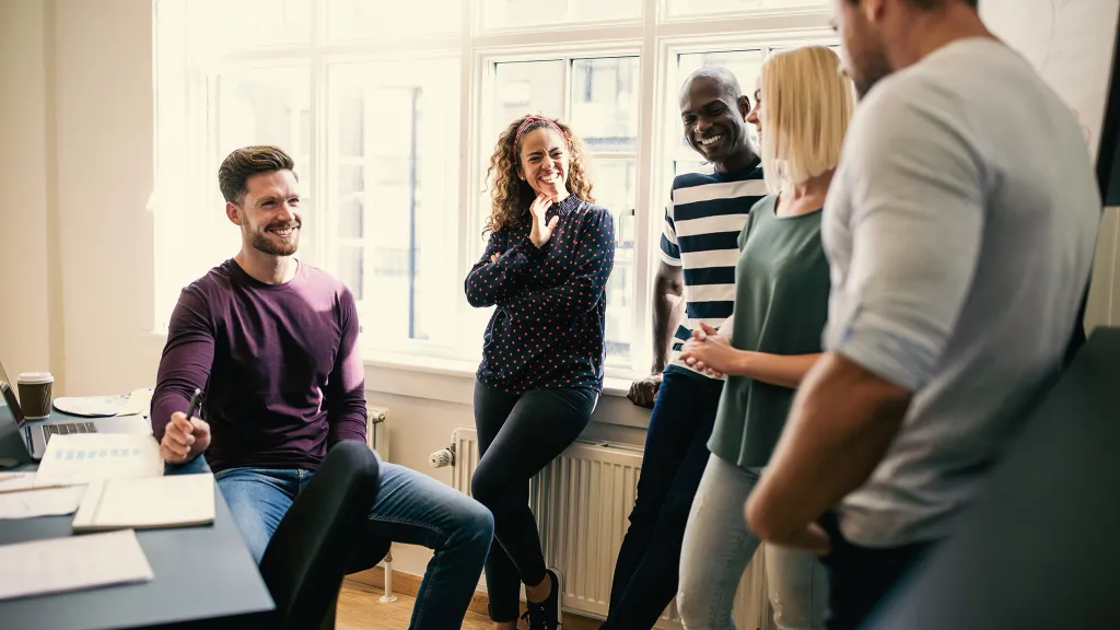 Five colleagues at work making small talk and laughing