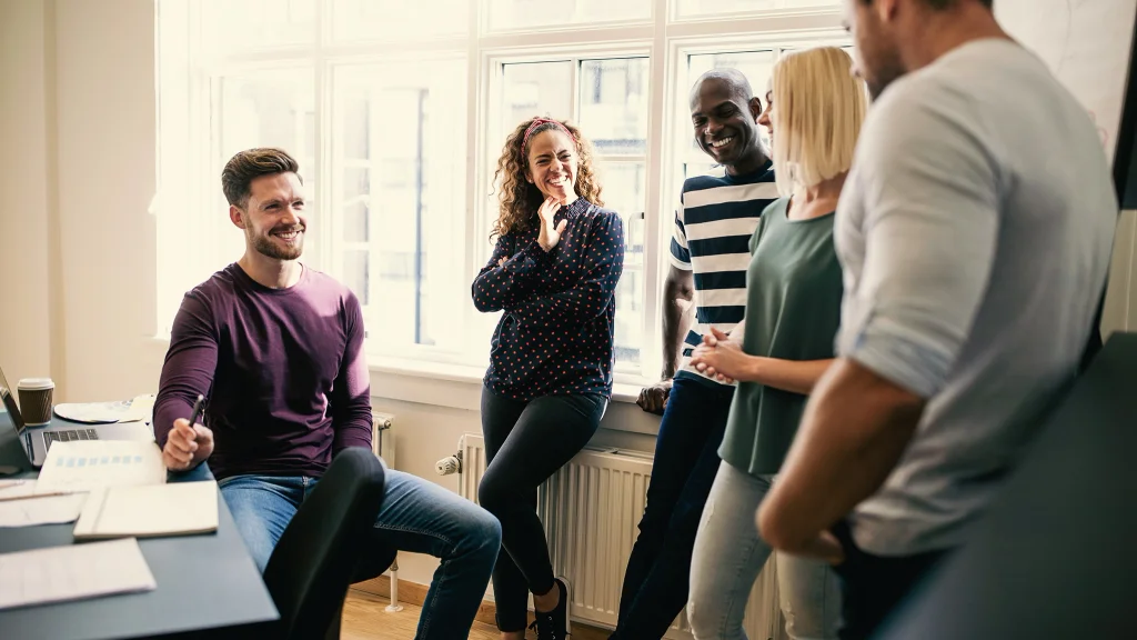 Five colleagues at work making small talk and laughing