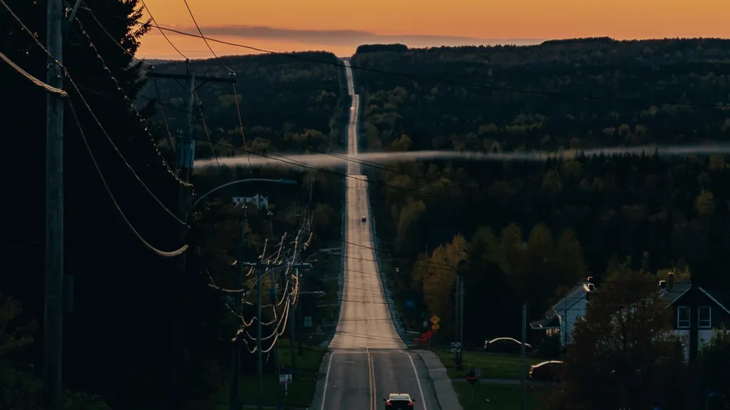 A card drives into the sunset on a long, hilly road.