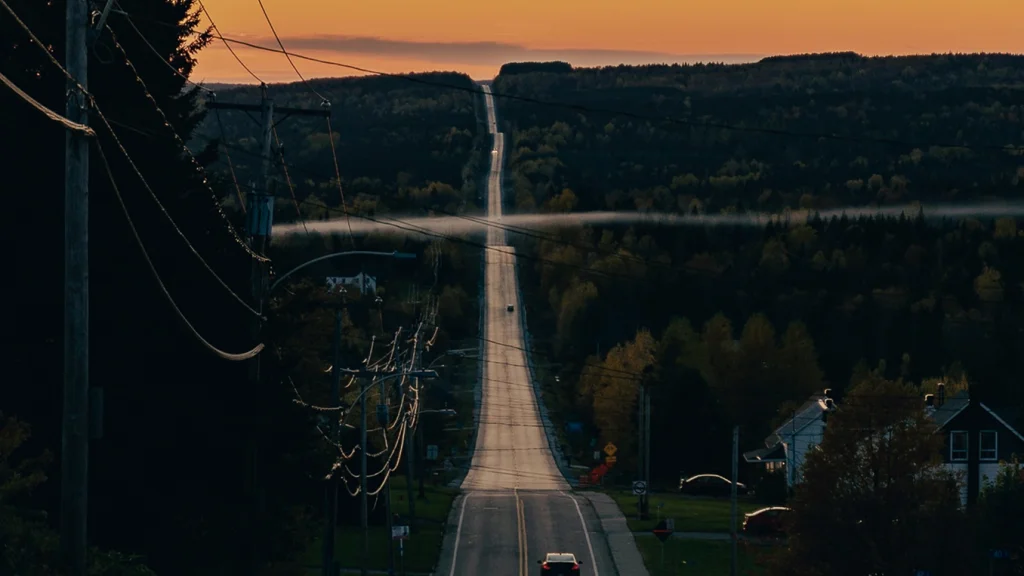 A card drives into the sunset on a long, hilly road.