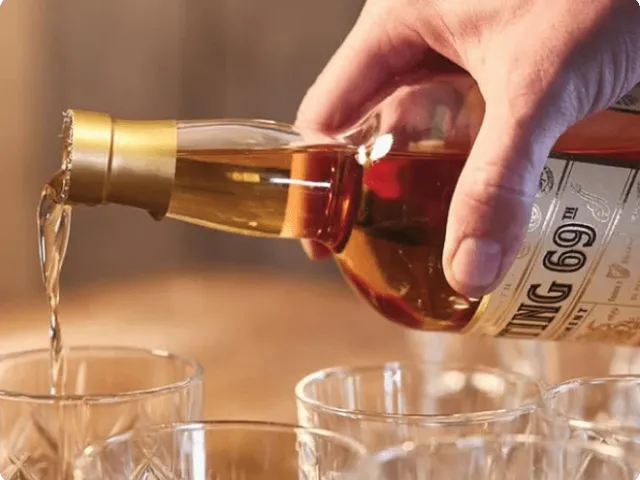 a hand pouring from a liquor bottle into glasses