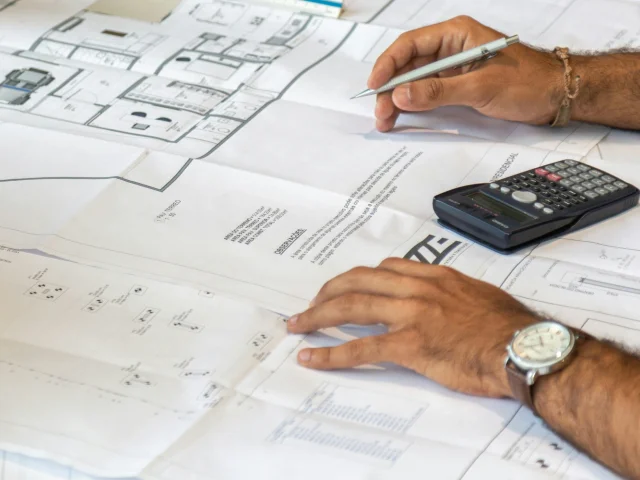 hands on top of mechanical drawings with calculator