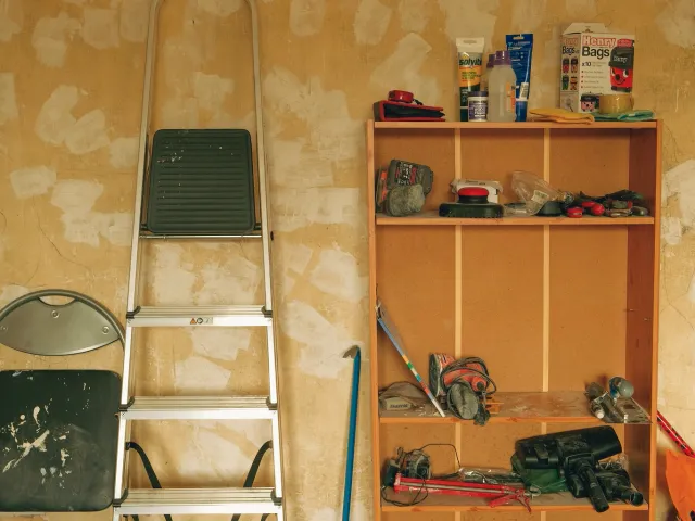 A wall with a ladder leaned up against it and shelving filled with tools