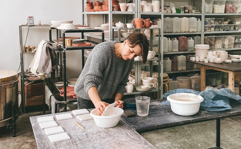 Small business owner glazing ceramic tiles in a pottery studio workshop.