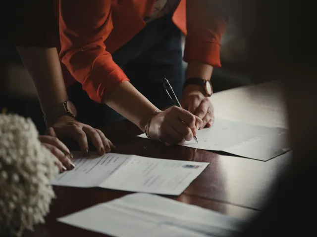 Two people bend over paperwork in a desk