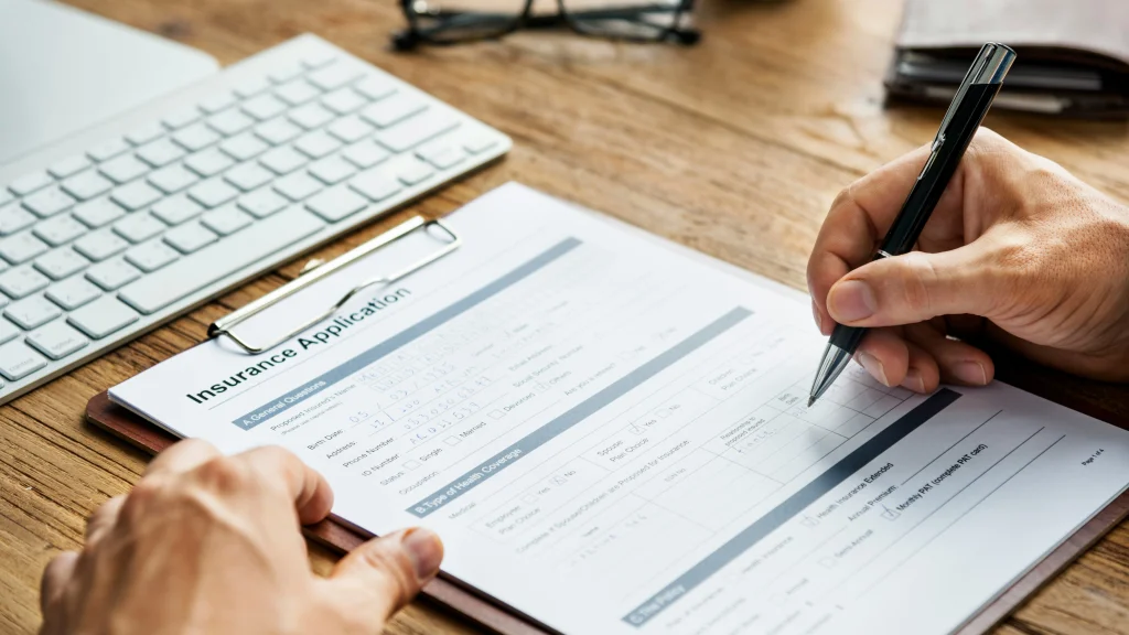 person filling out an insurance form on a clipboard