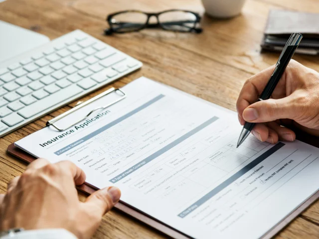 person filling out an insurance form on a clipboard