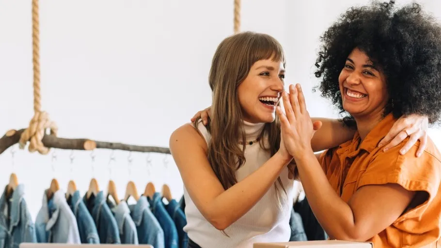 Two women small business owners high-fiving in their retail store