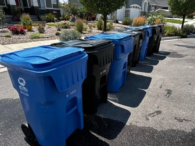 A row of recycling and trash bins in front of a house