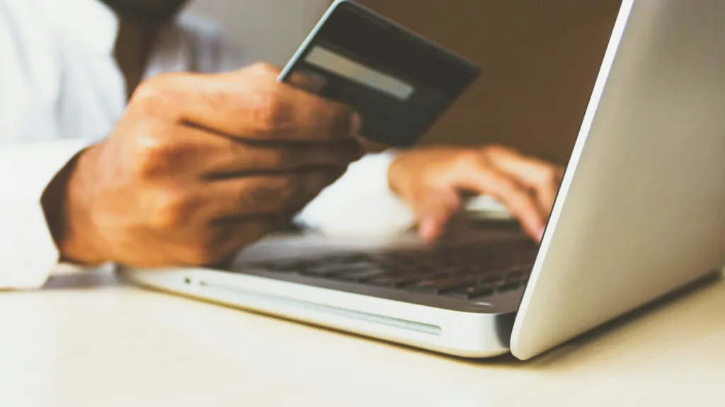 A hand holding a credit card and typing with the other hand into a laptop