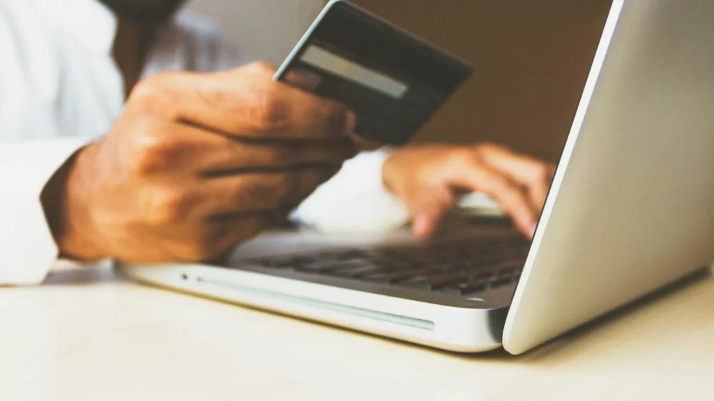 A hand holding a credit card and typing with the other hand into a laptop
