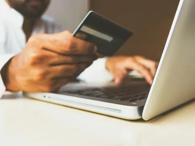 A hand holding a credit card and typing with the other hand into a laptop