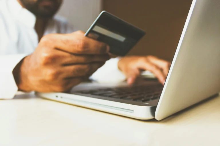 A hand holding a credit card and typing with the other hand into a laptop