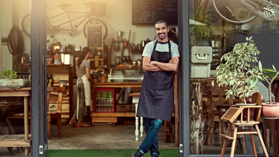 man standing with apron in front of a restaurant front