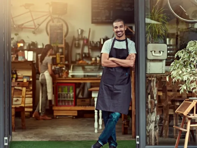 man standing with apron in front of a restaurant front