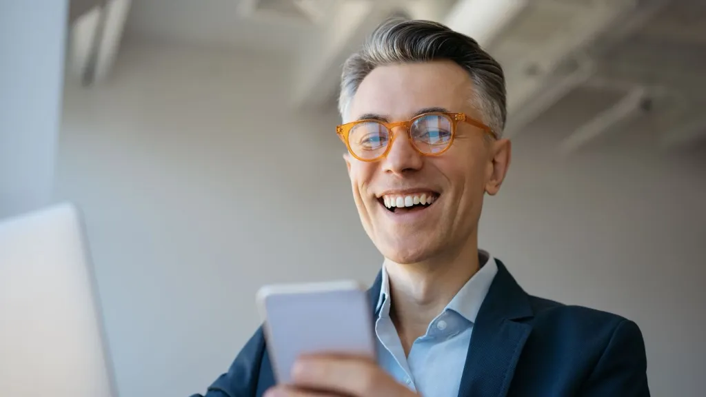 man wearing glasses in suit smiling while looking at cell phone to illustrate article about Nav vs WalletHub