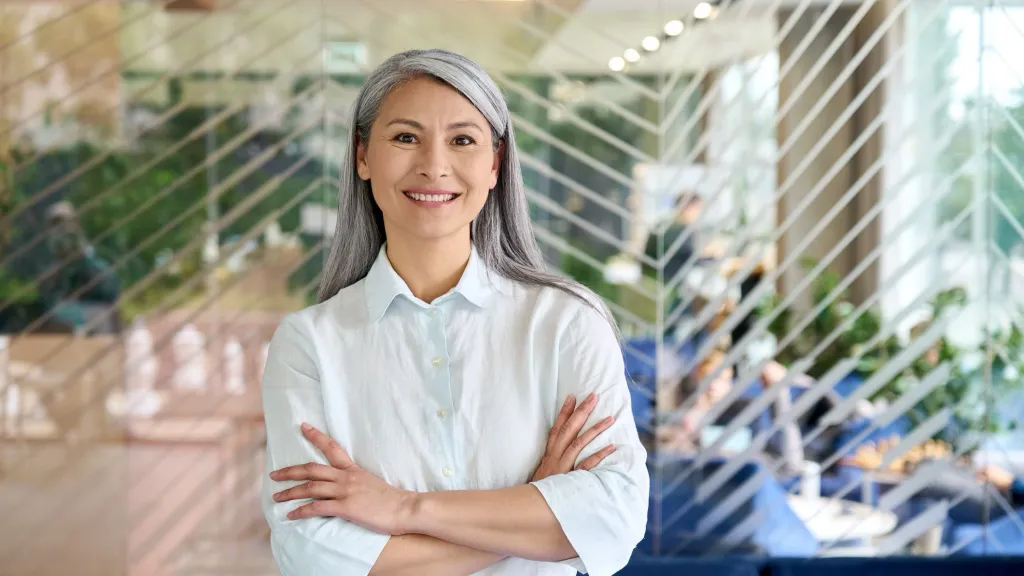 Professional woman smiling at camera with arms crossed to illustrate article about ROBS plans for business financing.