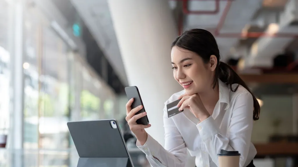 Photo of woman holding charge card looking at phone with tablet computer open to illustrate business charge card article