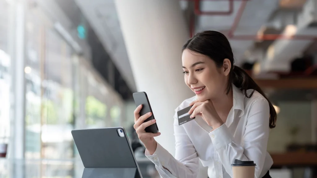 Photo of woman holding charge card looking at phone with tablet computer open to illustrate business charge card article
