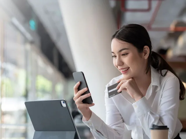 Photo of woman holding charge card looking at phone with tablet computer open to illustrate business charge card article