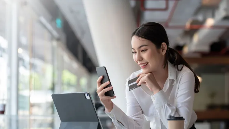 Photo of woman holding charge card looking at phone with tablet computer open to illustrate business charge card article