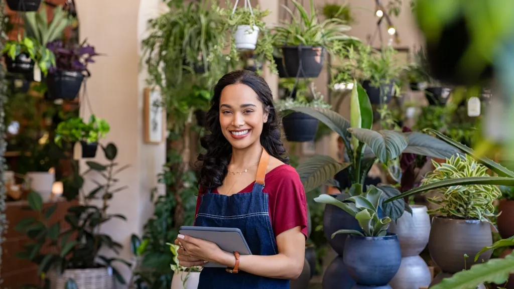 Woman business owner with tablet in shop surrounded by plants to illustrate annual business revenue
