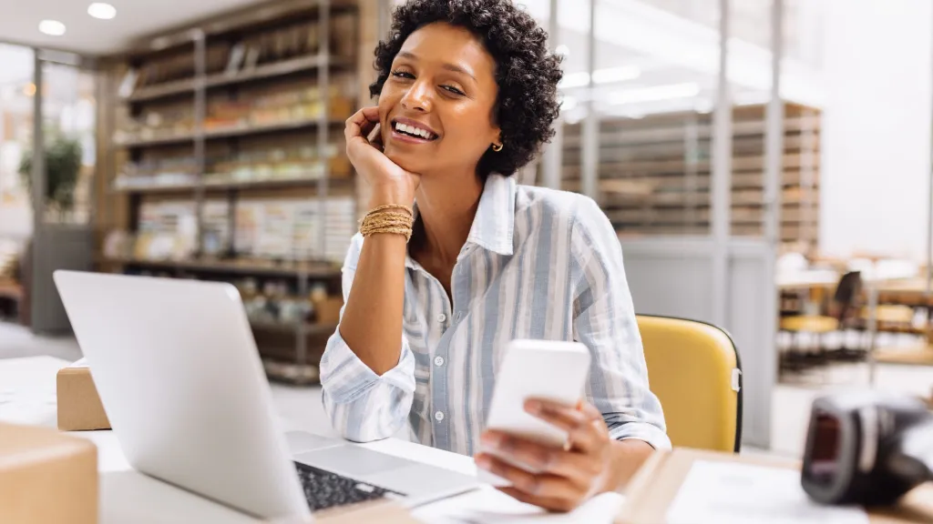 business owner smiling with laptop and cell phone to represent checking business credit