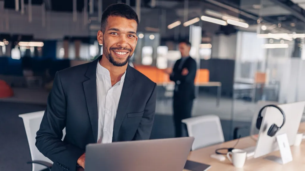 Businessman with laptop looking in camera and smiling to illustrate article about filing BOI report