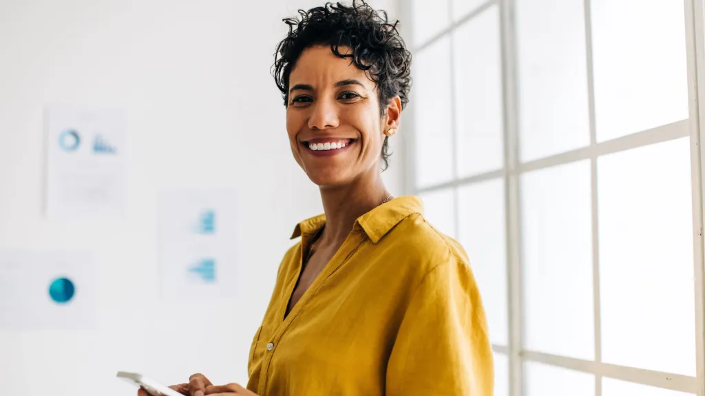 Woman smiling holding a cell phone to illustrate article about business credit monitoring