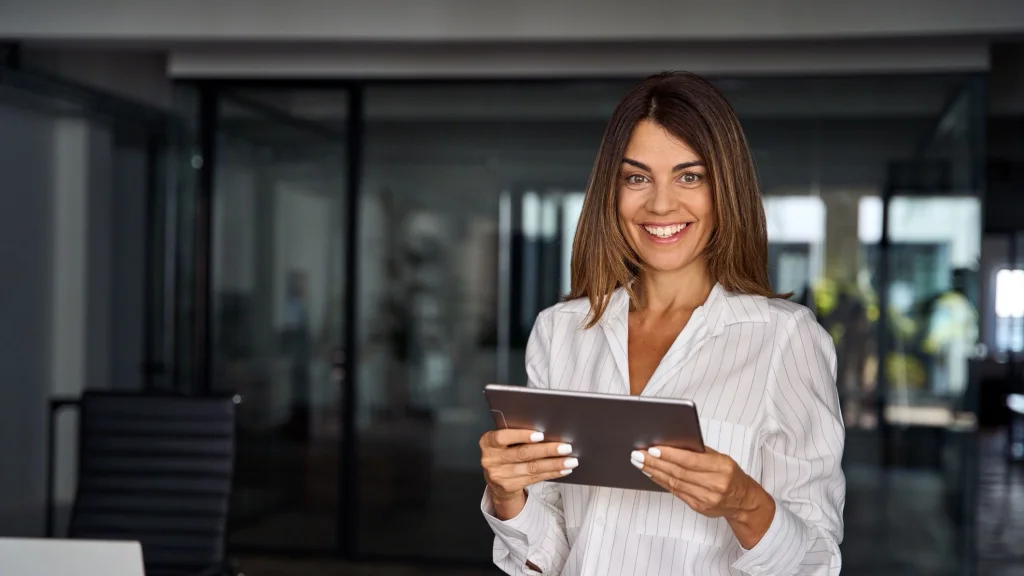 Woman in white top with long brown hair holding tablet to illustrate article about setting business financial goals.