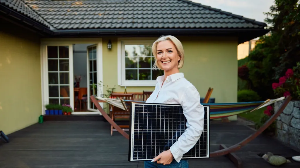 Smiling woman holding construction supplies in front of home to illustrate article about hard money loans and business credit.
