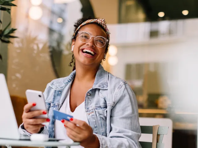 Smiling woman with credit card and cell phone to illustrate article about credit cards for startups