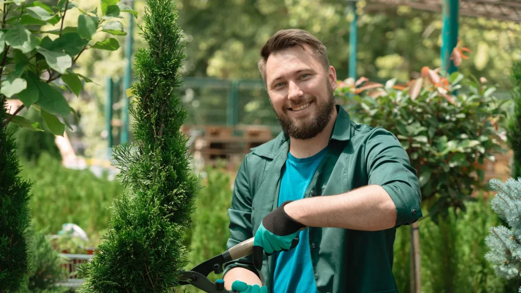 Man holding clippers standing in garden surrounded by bushes to illustrate article about pricing for service businesses