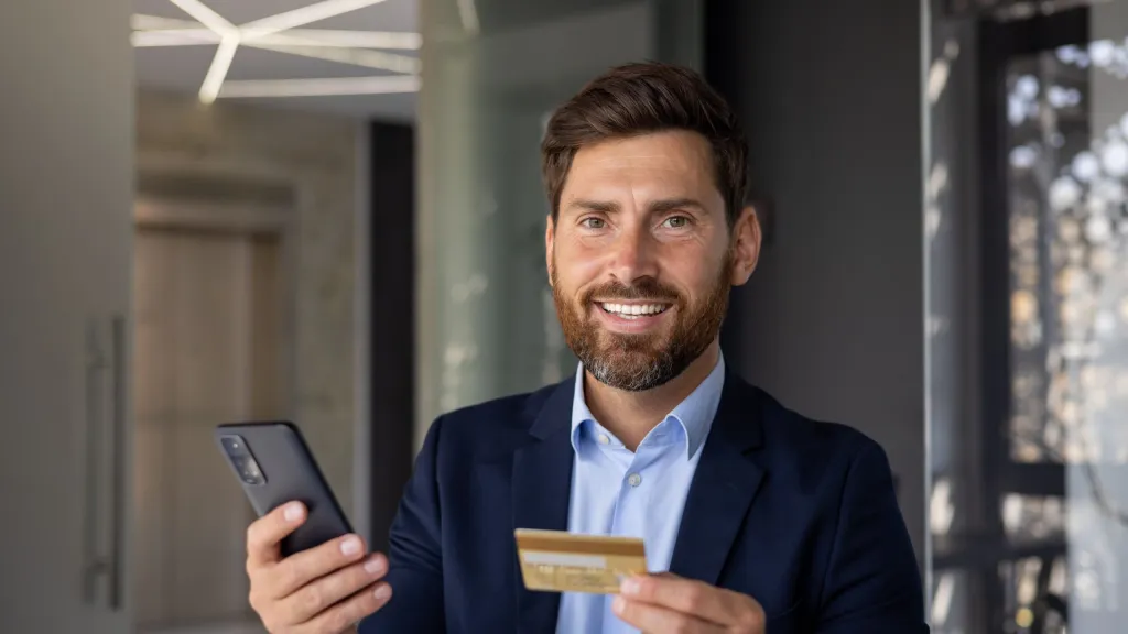 Professional in suit smiling holding a credit card and cell phone to illustrate article about easiest business credit cards to get