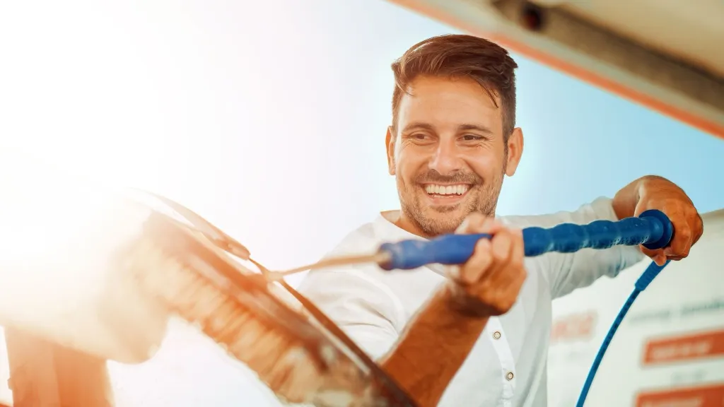 Man with dark hair and beard in dark shirt pressure washing to illustrate article about starting a pressure washing business.