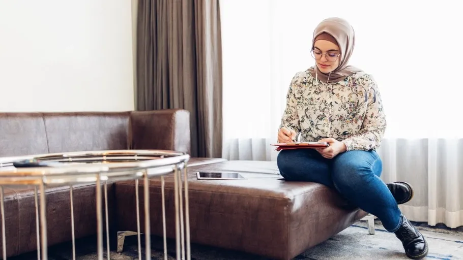 woman with headscarf filling out papers on a couch