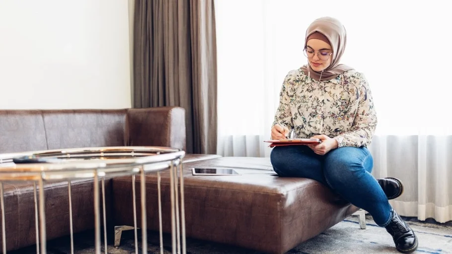 woman with headscarf filling out papers on a couch