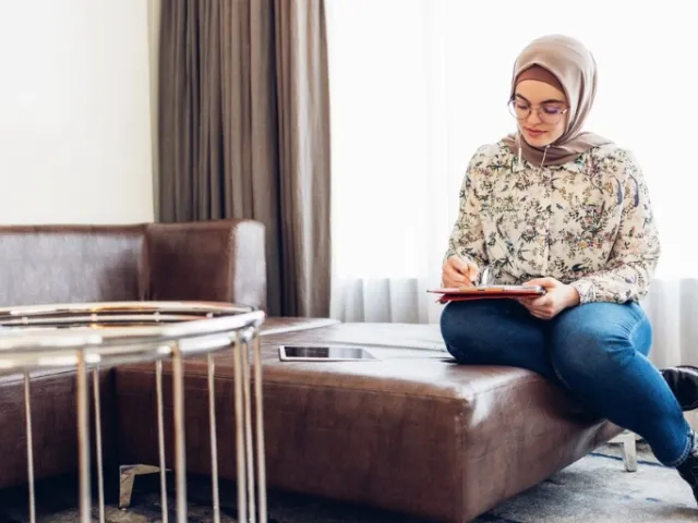woman with headscarf filling out papers on a couch