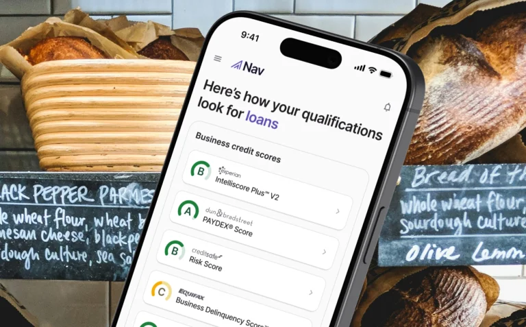 Smartphone displaying the Nav mobile app showing business credit scores and loan qualifications overlaid on a bakery shelf background.