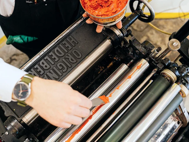 Person applying orange ink to the rollers of an Original Heidelberg letterpress printing machine